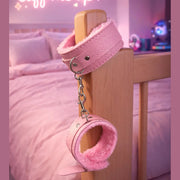 Cavigliere bondage rosa in similpelle appese a un piede di letto con segnale neon 'cuff me up'