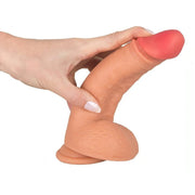 Mano che stringe dildo in silicone morbido rosa carne per mostrare flessibilità e texture scrotale